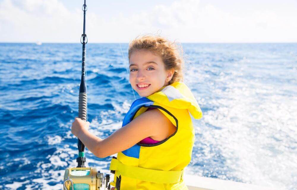 Young girl fishing with rod and reel in yellow life jacket